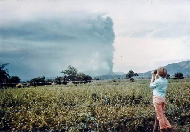 A young girl observes a volcano errupting through binoculars