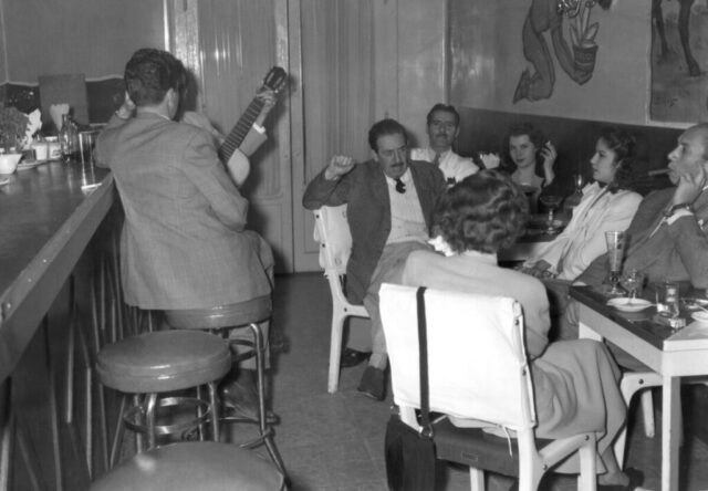A group of people drink, smoke, and listen to musicians at George the Greek’s bar in Mexico City, México, 1948. ©KMC