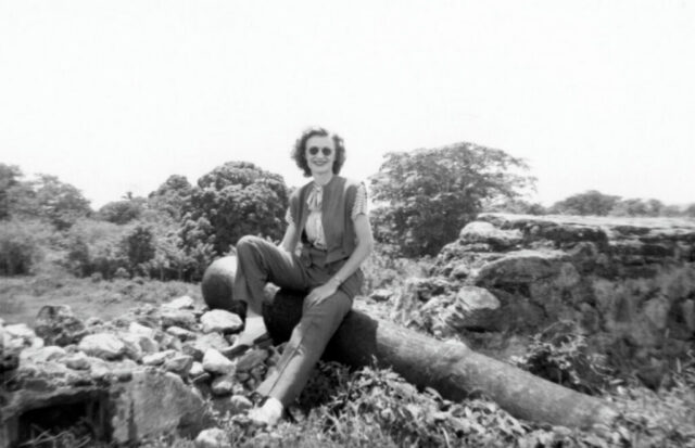 A young woman sits on what looks like an old cannon in a crumbling fortress wall, c 1944. ©KMC