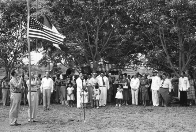 A group of people watch as the US and Mexican flags are raised and a band plays during a 4th of July picnic in Tampico, México, 1953. Foto Martinez