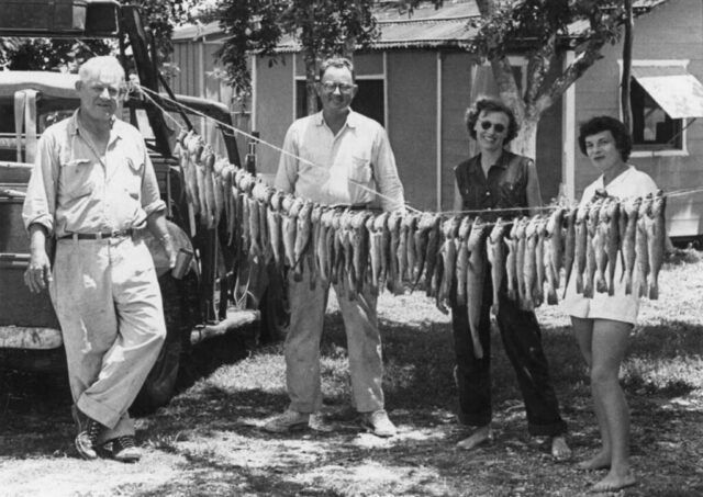 Four people stand beside a long string of fish caught at Barra de Chevarría. Tampico, México, 1954. ©KMC