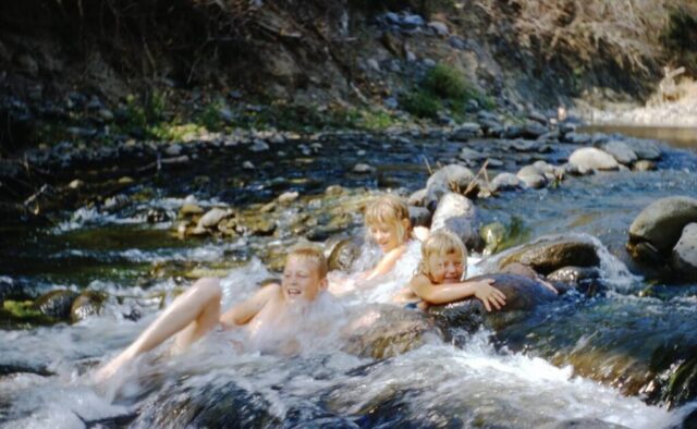 Three kids slide down a rushing creek, Río Los Plátanos, Guatemala, 1958. Jack, Judy, and Linda. ©KMC