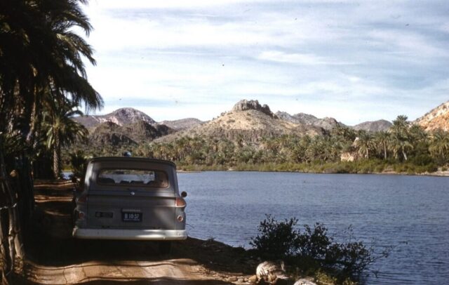 The carryall is stopped on a dirt road bordering a deep blue estuary in a vibrant palm oasis, Mulegé, Baja California Sur, one of the most beautiful spots in Baja California, 1961. ©KMC