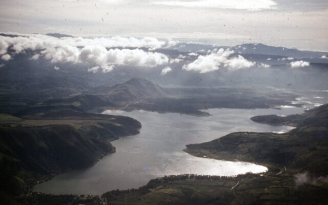 Arial view of an expansive lake surrounded by mountains and covered with scattered clouds. Lago de Amatitlán from 10,000 ft, 1958. ©KMC