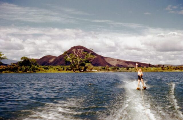 A boy is waterskiing and waving his hand behind a boat. Jack on Lago de Amatitlán, 1959. ©KMC