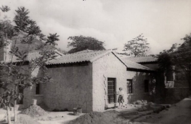 A woman in a skirt stands at the door of a terra cotta tiled house in Tegucigalpa, Honduras, 1947. ©KMC