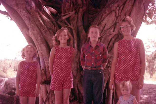 Three girls dressed alike and ranging in age pose with a boy and a young child in front of a huge tree. Last day in Guatemala. Río Naranjo, 1960. ©KMC