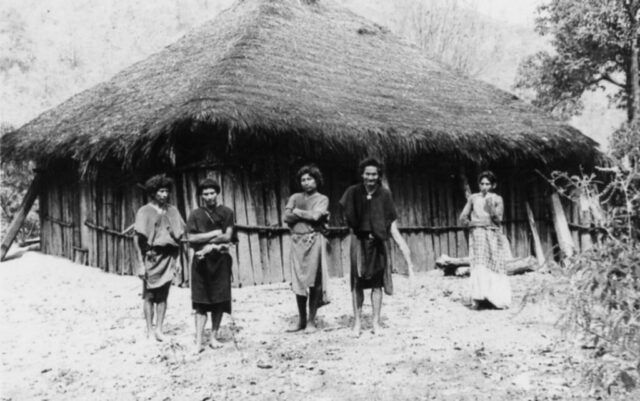 Indigenous people stand in front of a thatch roofed hut in Honduras, 1946. ©KMC